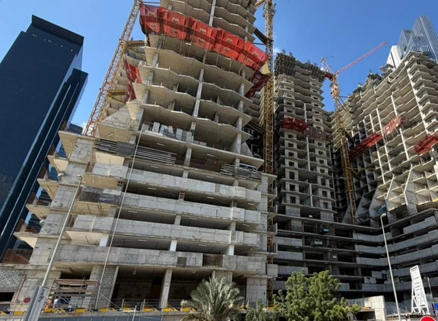 Multi-storey concrete residential towers under construction with tower cranes and safety netting