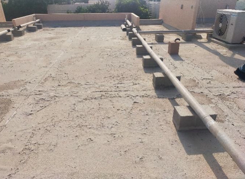 Villa rooftop with pipework raised on concrete blocks, parapet walls and an AC condenser unit