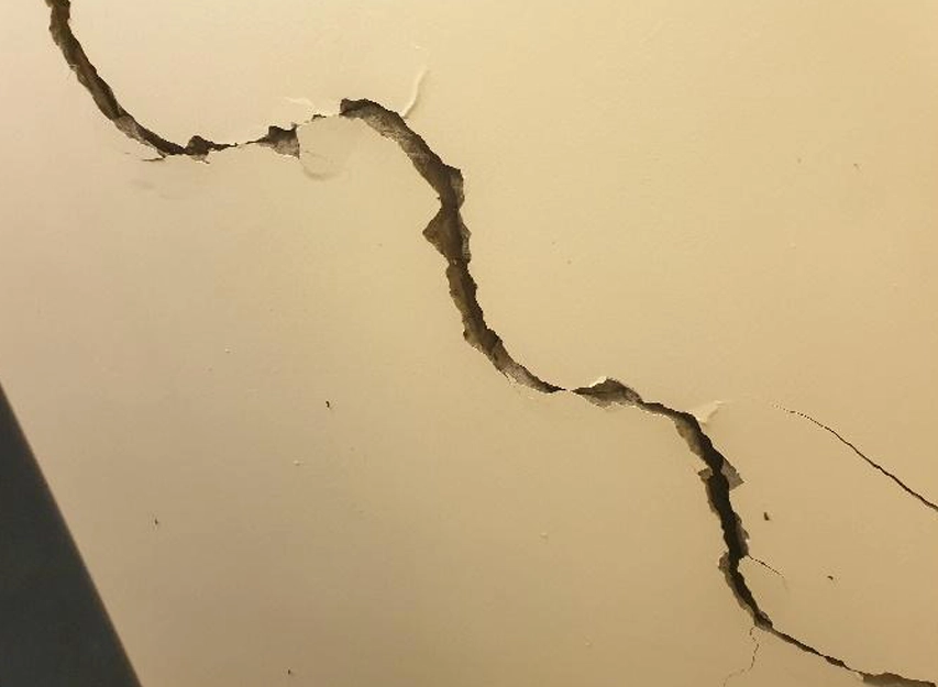 Close-up of a wide diagonal crack in a painted wall surface