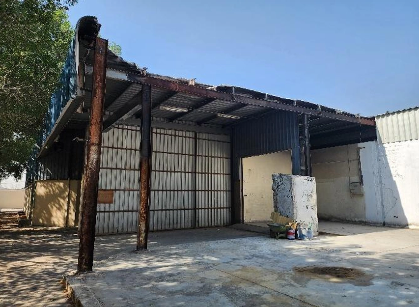 Warehouse exterior with a collapsed, burnt roof edge and rusted support posts