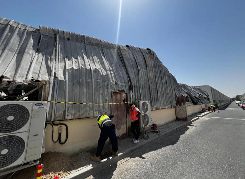 Two workers inspecting a warehouse roof with buckled, fire-damaged corrugated sheeting