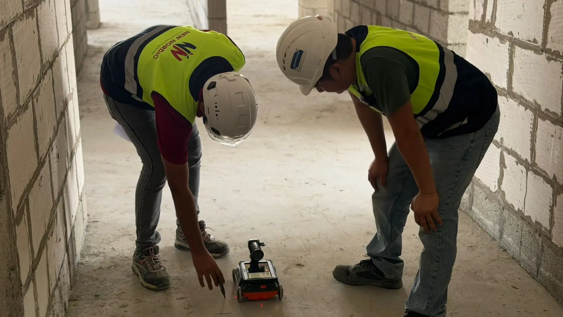 Two New Nordic engineers examining a ground penetrating radar scanning device in an unfinished corridor