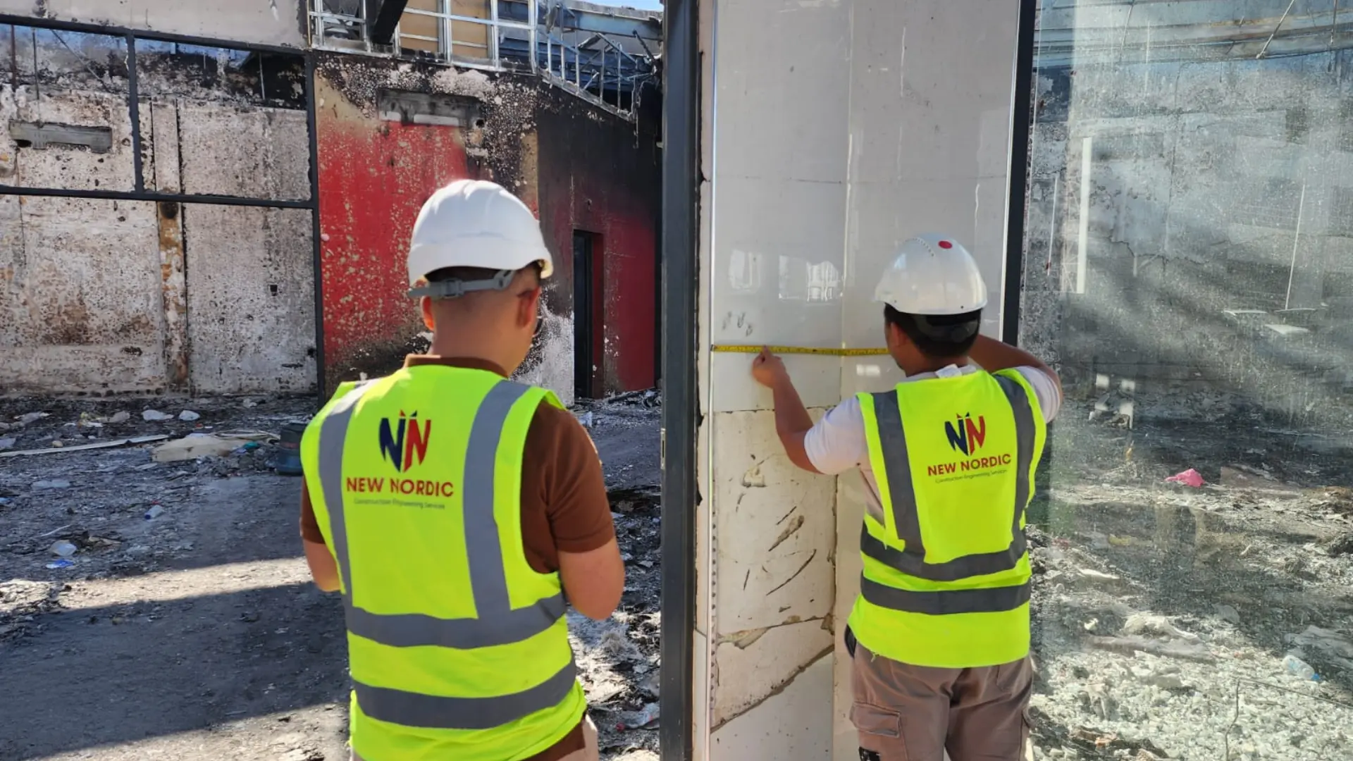 Two New Nordic engineers measuring a fire-damaged wall with a tape measure at a burnt building