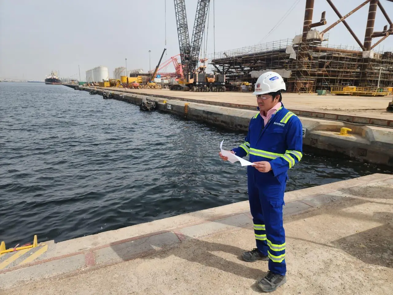 New Nordic engineer reviewing inspection documents on a quay beside open water at a UAE port