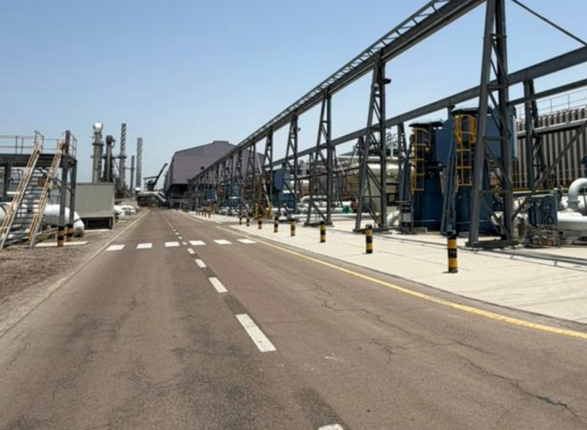 Road running through an industrial plant past steel gantry and conveyor structures