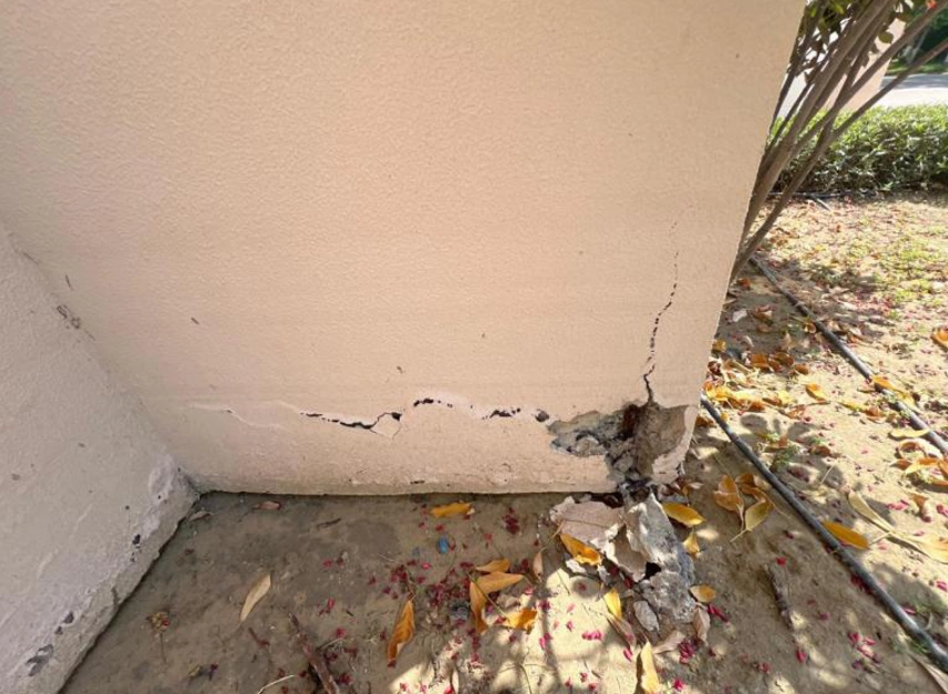 Cracked and spalled concrete at the base of an exterior rendered wall