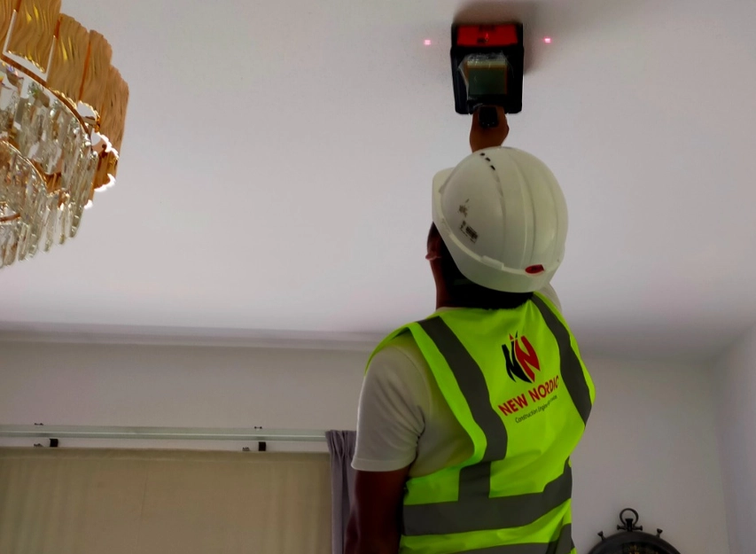 New Nordic engineer using a handheld leak-detection device on a ceiling in a furnished room