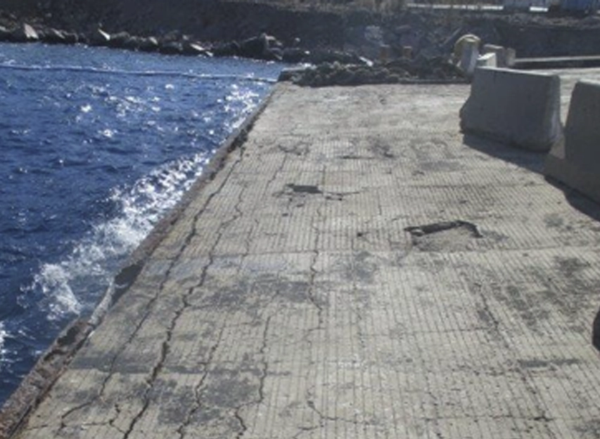 Cracked and patched concrete jetty deck beside the sea with concrete barriers